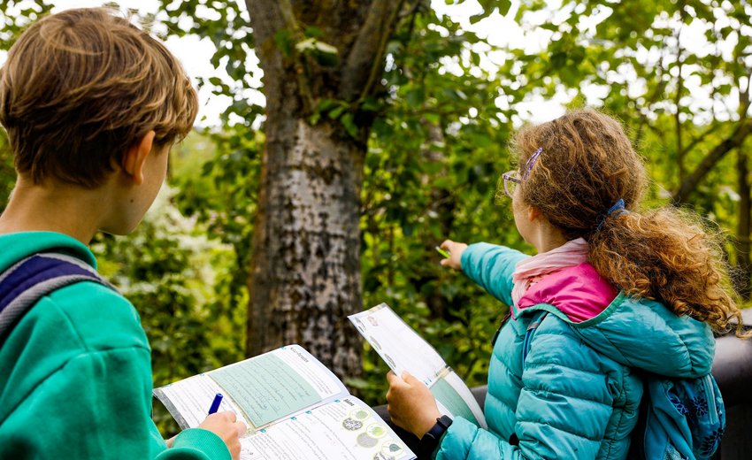 Zwei Kinder stehen vor einem Baum und füllen ein Rallyeheft im Natur Park Südgelände aus